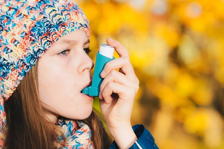 Asthma patient girl using inhaler in park. Asthma concept.