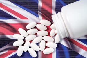 White pharmaceutical pills spilling from prescription bottle over British flag. Brexit concept. SCAIR.