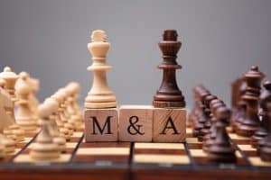 chess pieces mounted on scrabble squares spelling M&A, illustrating mergers and acquisitions concept