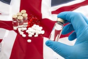 A gloved hand holding a vial of pills against the union jack flag. Concept showing UK drugs shortage