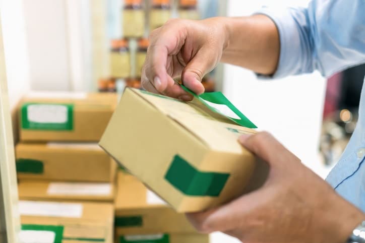 Hand affixing label to cardboard box containing drug supplies.