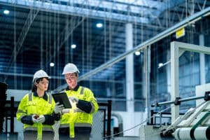 Male and female engineers in neat work clothes prepare and control the production system of large modern machines in a factory producing industrial technology products. Image for SCAIR blog on the UK's industrial strategy.